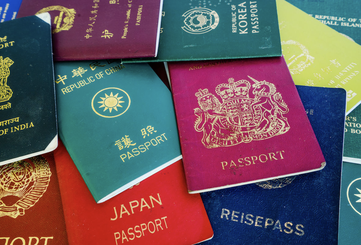 A high-angle, close-up shot of several international passports from different countries, including India, Japan, the Republic of Korea, and the United Kingdom, scattered in a colorful pile.